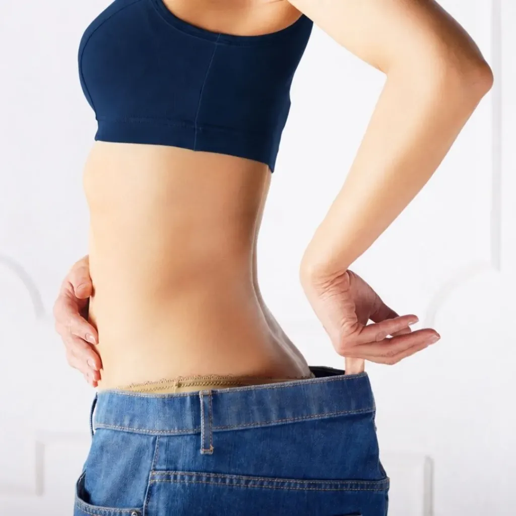 Close-up of a woman's midsection with hand at her waistband, weight loss imagery