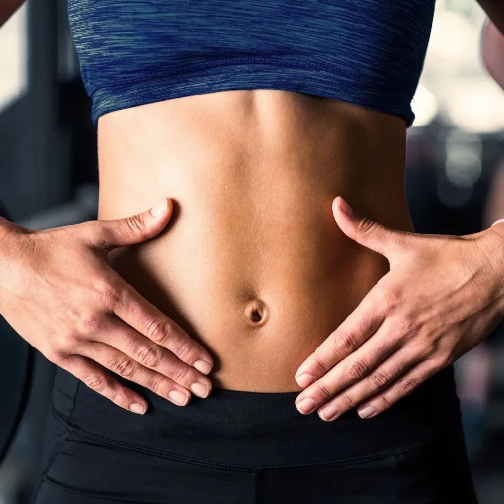 Close-up of a woman's toned midsection with hands resting on her stomach